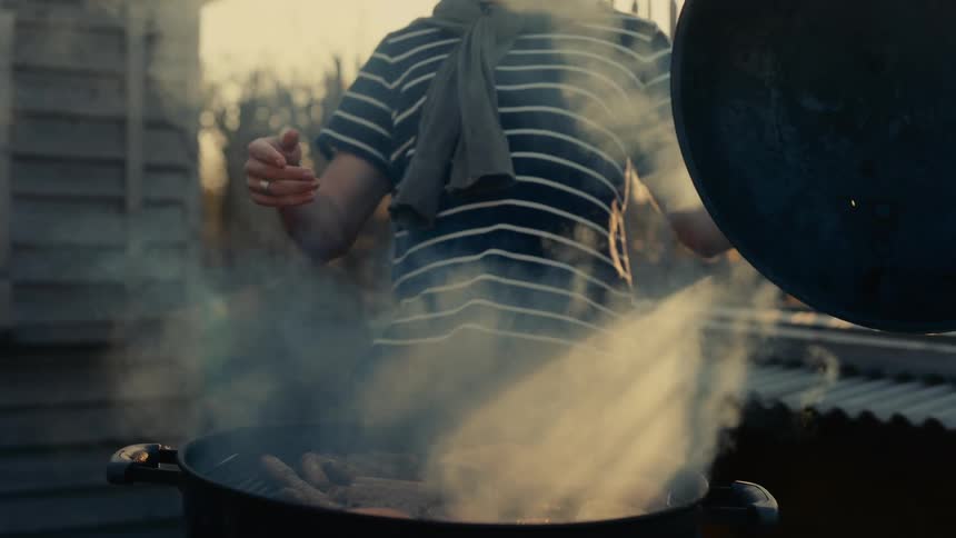 Person opening the drum of a barbecue while grilling meat in the late afternoon