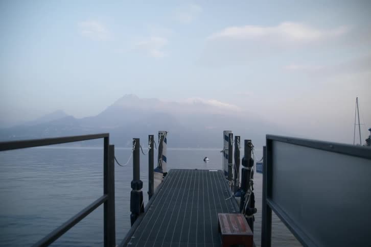 A small pier made of a metal structure with metal handrails and in front there is a large lake with a mountain looming in the background