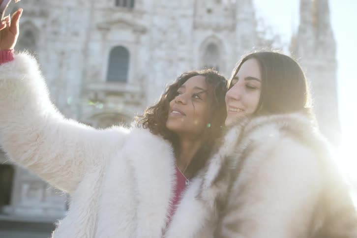 Two girls in furry coats taking a selfie in front of a castle