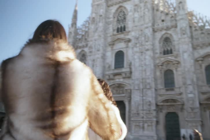 Two women are holding hands as they spin in front of a gothic church