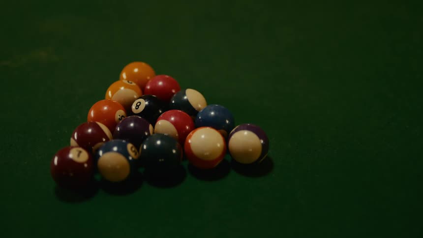 Several billiard balls on a green table are hit by another ball and scattered