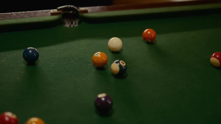 A cue ball knocks a maroon billiard ball on a green table