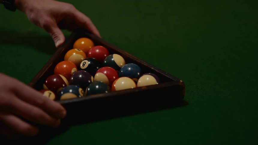 A person is arranging a set of billiard balls in a triangular rack on a green pool table