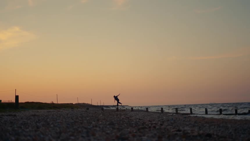 Silhouette of a person balancing on a wooden stump on the beach