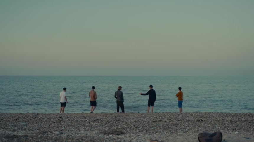 Five men on the beach throwing stones into the sea