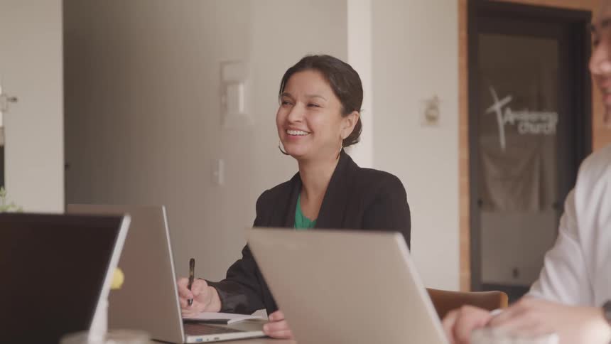 Coworkers smile while sitting in a meeting with their laptops