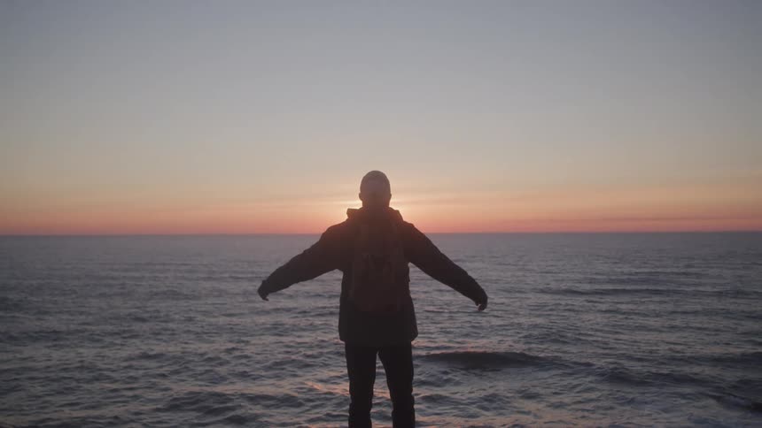 Man opening his arms facing the ocean at sunrise