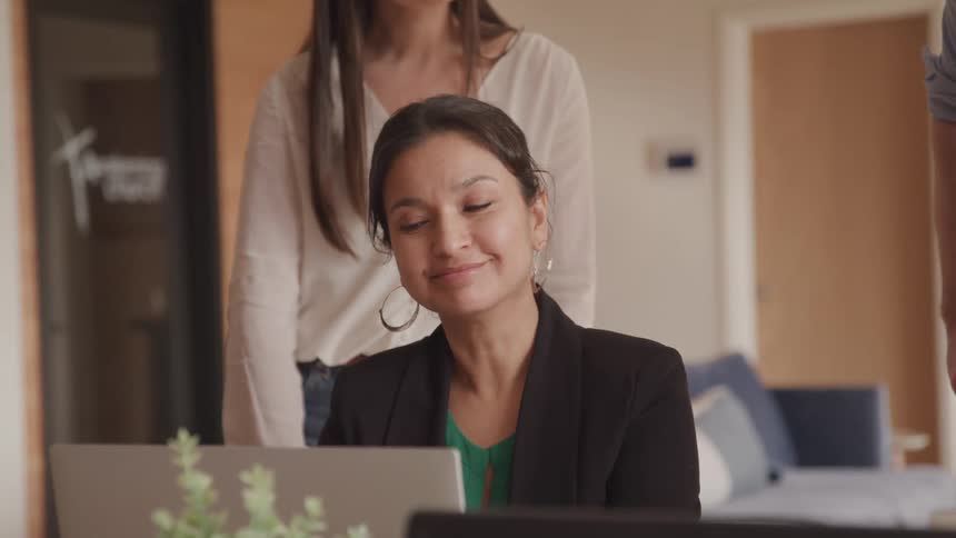 A footage of a woman sitting in the office and smiling while having a conversation with others