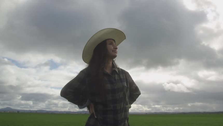 Woman wearing a hat and standing in a farm field with her hands on her hips
