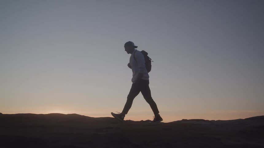 Man in cap and backpack walking on a rock at sunrise