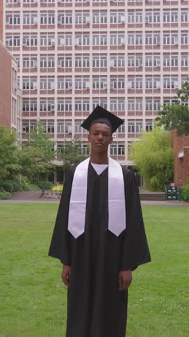 Young man in graduation gown in a garden facing the university