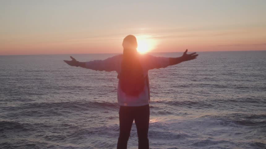 Traveler with open arms by the sea and the reflection of the red sun rising on the horizon