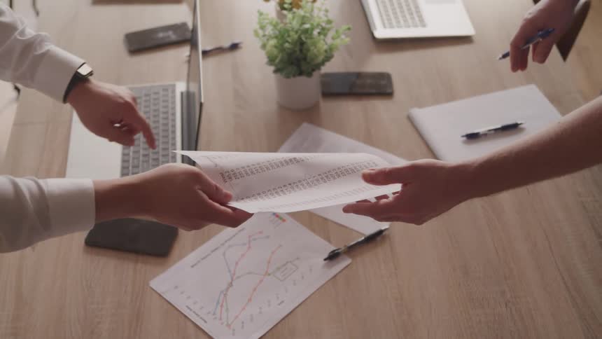 Pair of hands handing paper in a document to another person on a table