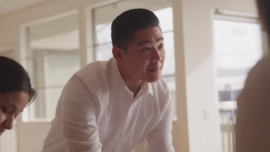Man surrounded by other people at an office desk talking