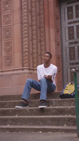 Student sitting on the outside stairs of a university while writing in a notebook