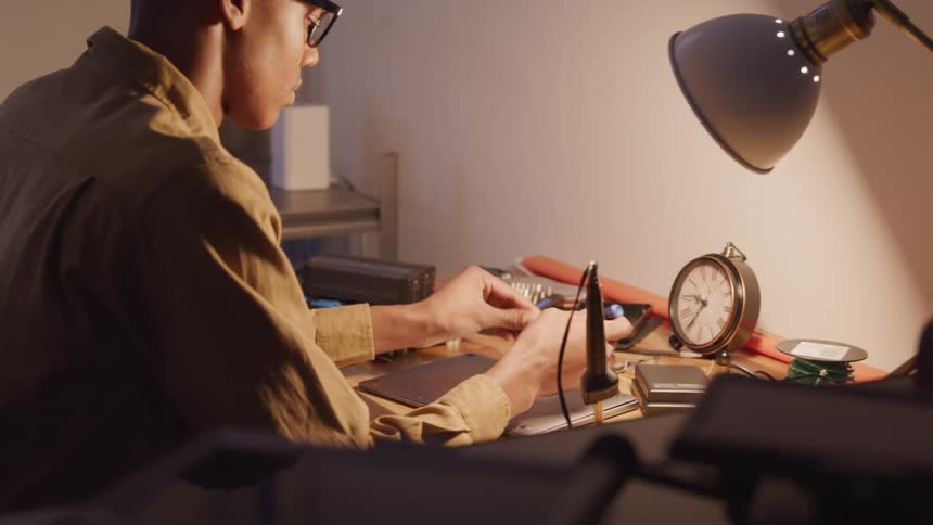 Young man sitting at a table using a tool and opening the back of a laptop