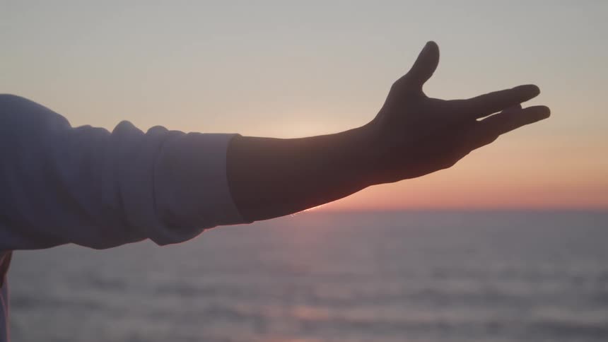 Arm rising in a seaside setting with the sun rising on the horizon