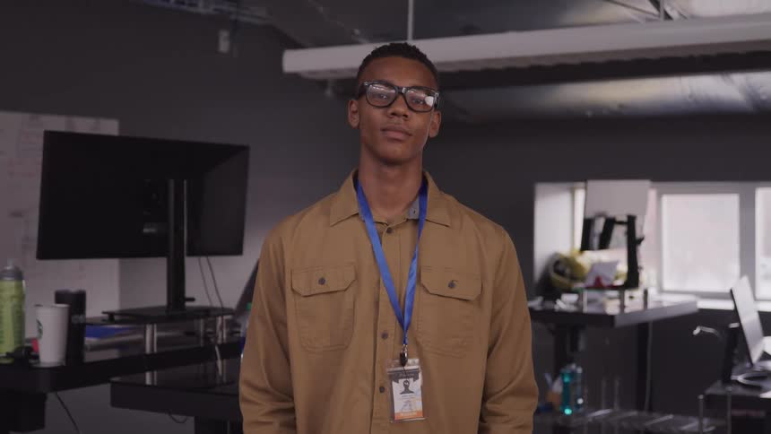 Man in glasses standing at a desktop with a badge on his chest