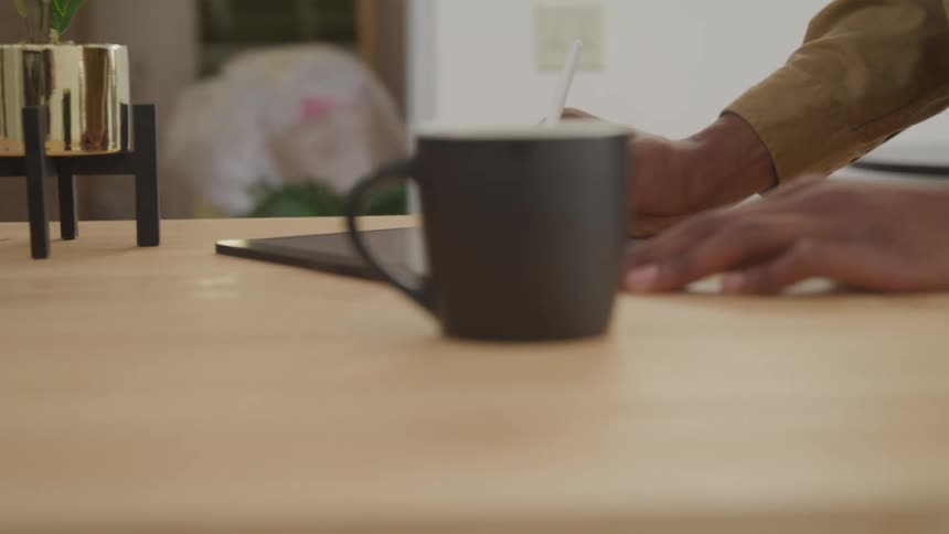 Pair of hands with a digital pen interacting with a tablet on top of a wooden table