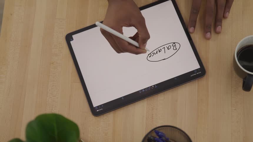 Person sitting at a table draws a diagram on a tablet using a stylus