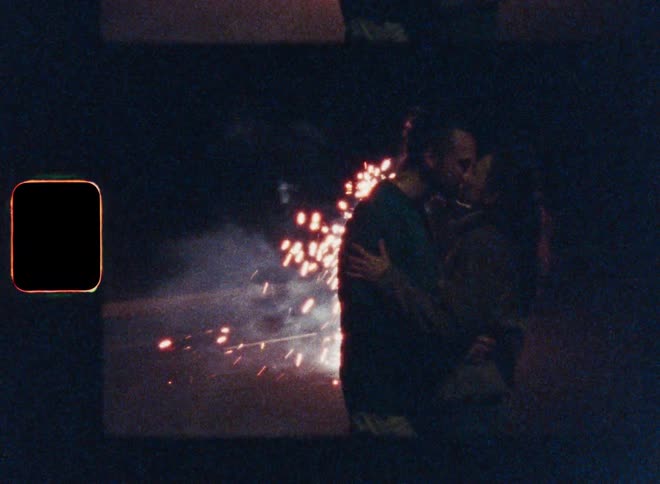 A man and a woman kissing outdoors with several sparks shining behind them