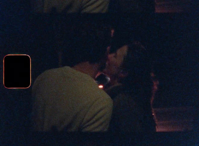 Woman kisses a man as they stand outdoors at night near sparking fireworks