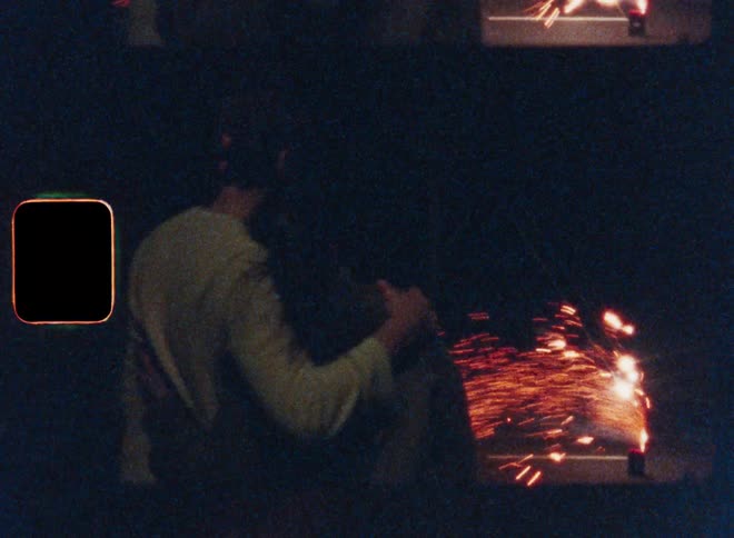 Couple hugs while watching fireworks spark on the pavement at night
