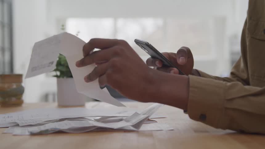A person scans or photographs a receipt with a smartphone surrounded by other receipts and papers on a table