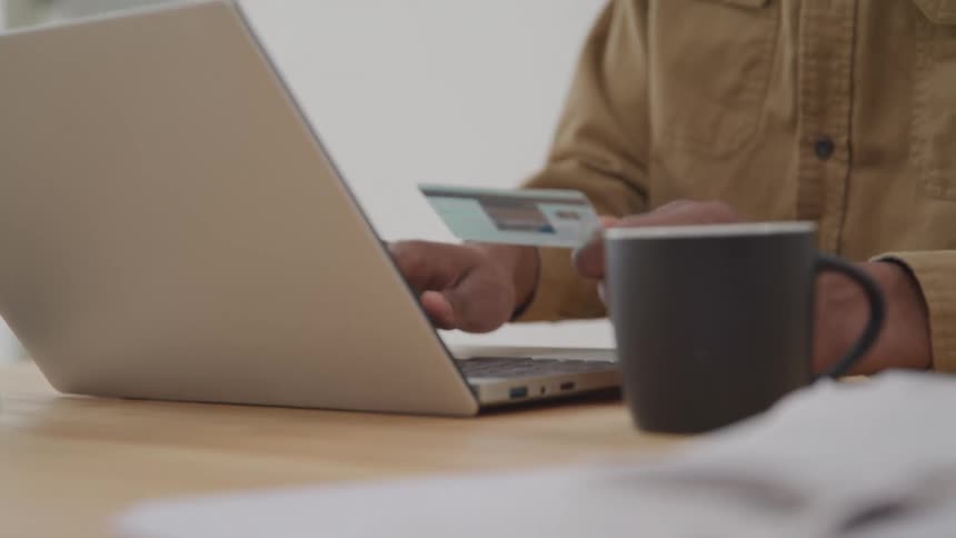A person holding a credit card with one hand and with the other is typing on a laptop keyboard