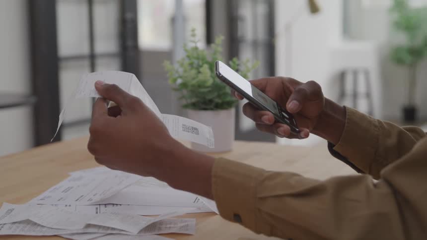 A person scans or photographs a receipt with a smartphone surrounded by other receipts and papers on a table