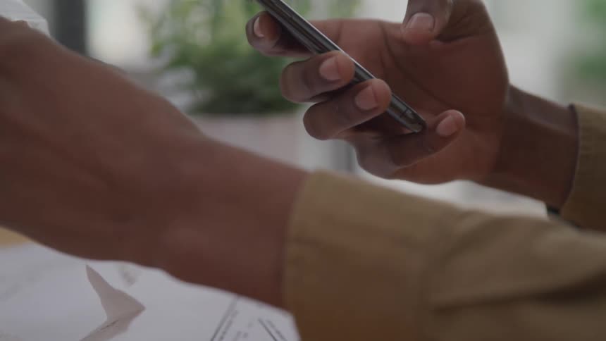 The hand of a person wearing longsleeved clothing who is typing on a cell phone