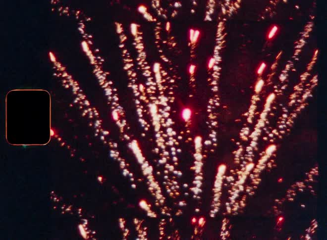 Against the deep darkness of the night brilliant bursts of light illuminate the sky as mortar shell fireworks explode in a dazzling display with trails of sparks radiating outwards captured through the nostalgic texture of analog film