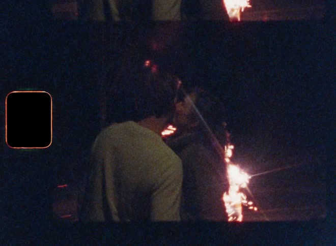 Man and woman kiss and hug while standing outdoors at night watching sparking fireworks