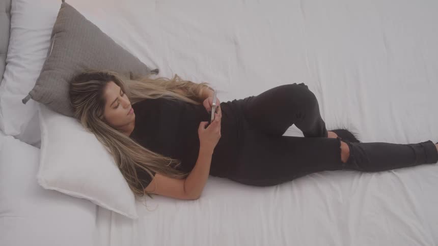 Woman lying in bed typing on a smartphone