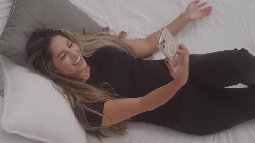 Cheerful woman lying on bed talking on video call