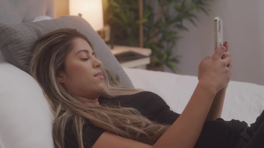A woman is texting on her phone in bed