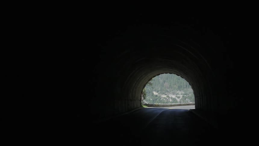 A vehicle drives through a tunnel besides hill and mountains