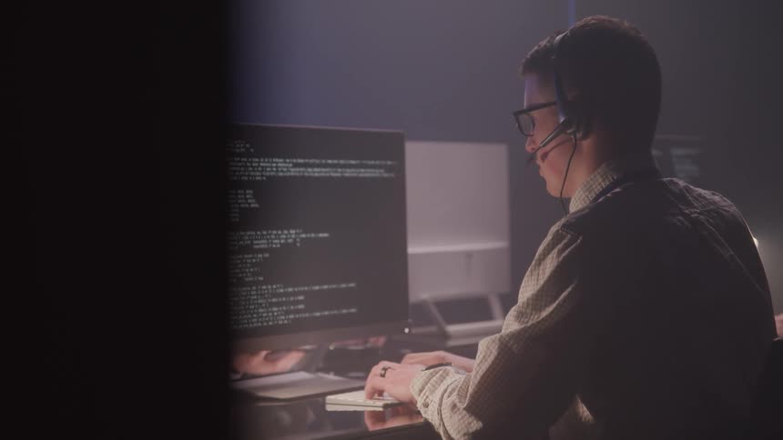 A man wearing a headset is typing on a computer at a desk
