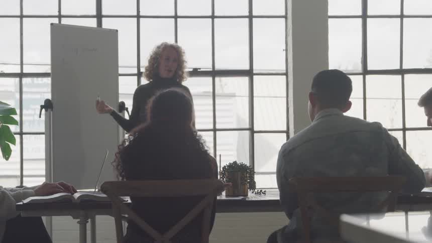 A woman writes on a board as she conducts a meeting
