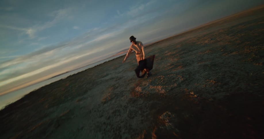 A person dances on a rocky beach nearby and a distant coastline under a sky streaked with clouds