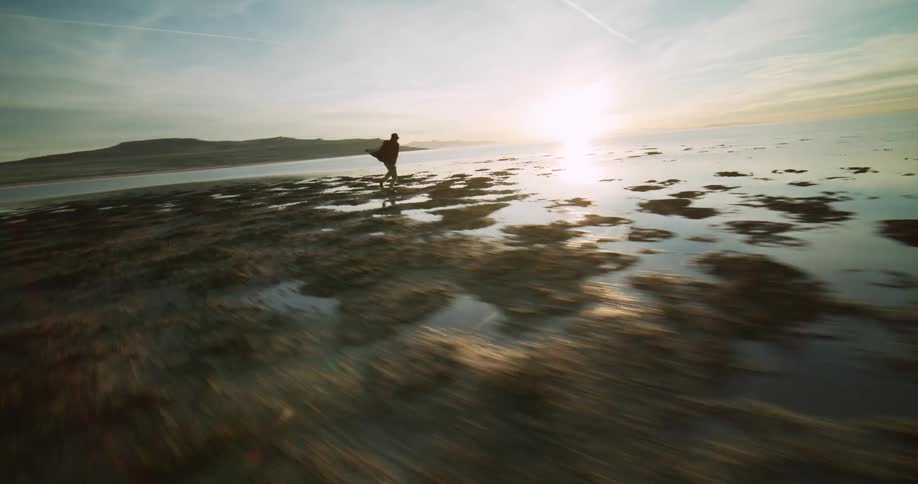A person dances on a rocky beach nearby and a distant coastline under a sky streaked with clouds