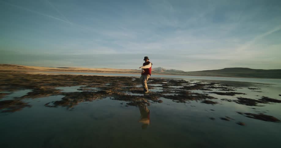 Aerial view of a man dancing on the shores of a marsh at sunset