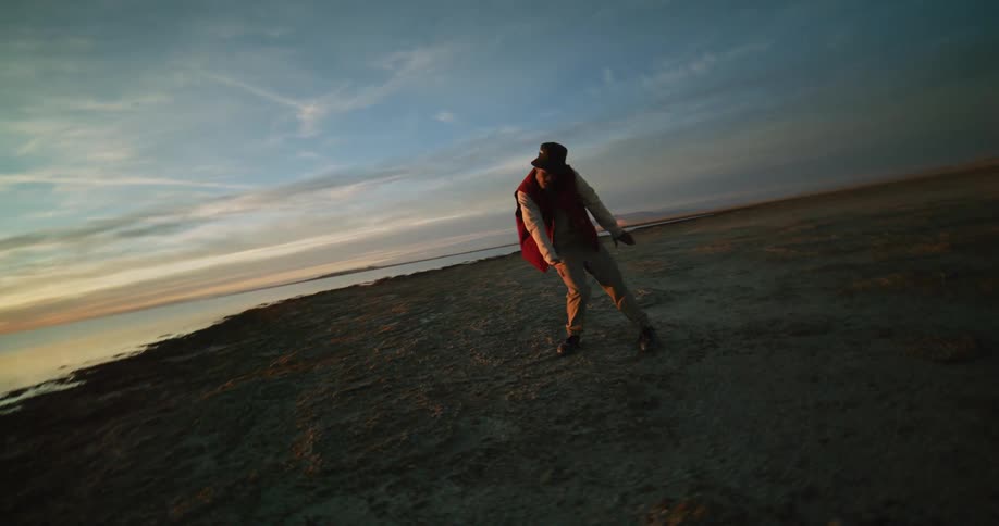 A man is dancing on a beach near the water
