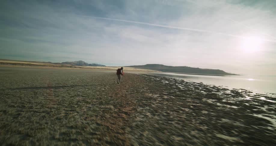 Man dances across a desert landscape near a body of water with the sun low on the horizon