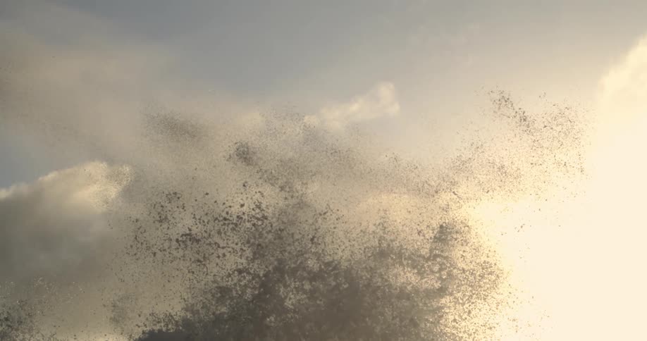 Sea spray bursts against a backdrop of a pale sky at sunset