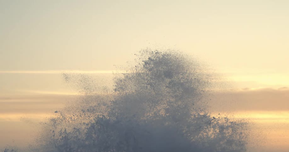 Sea spray bursts against a backdrop of a pale sky at sunset