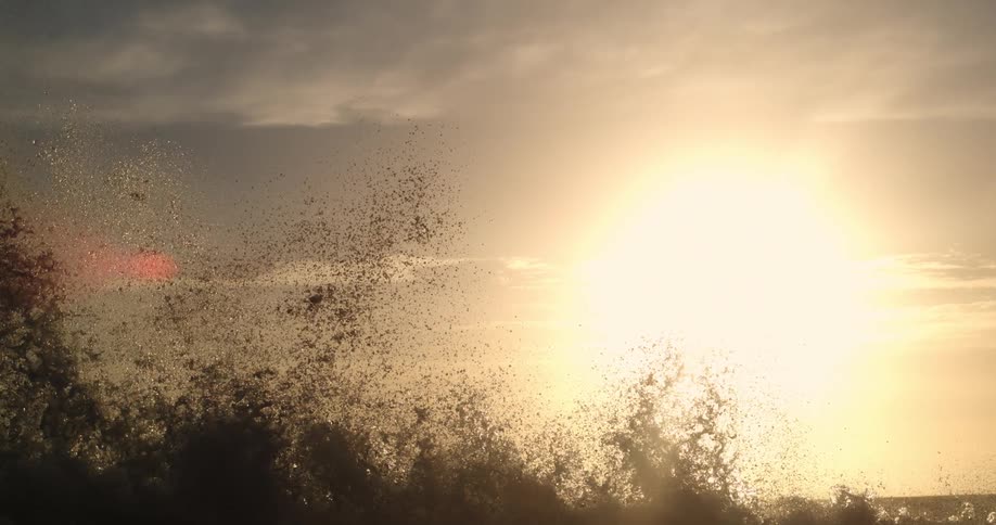 Waves crash with the sun shining brightly in the background