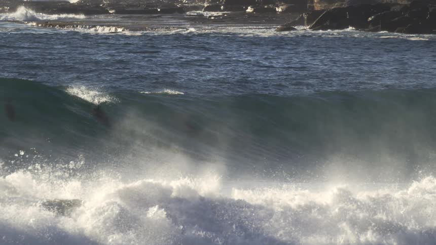 A medium wave rolls over and lands on a coast with cliffs