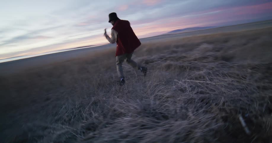 A man is dancing in the grass by the shore