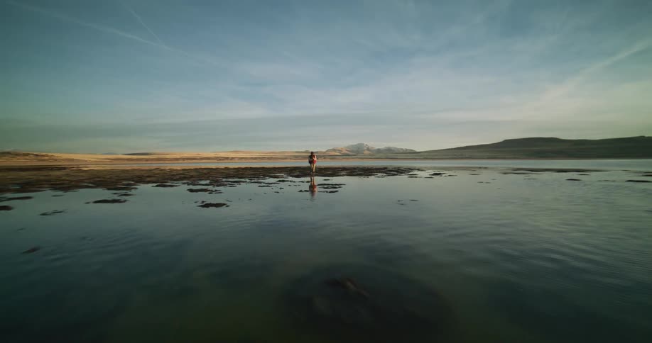 Man is dancing on the edge of a body of water with the sun in the background illuminating the scene